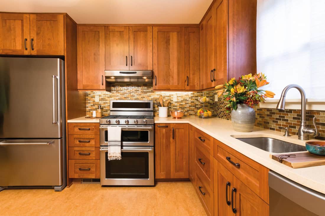 intérieur de cuisine à domicile avec armoires en bois de cerisier, comptoirs en quartz blanc, sols en linoléum recyclé durable et appareils en acier inoxydable, y compris réfrigérateur et cuisinière à gaz
