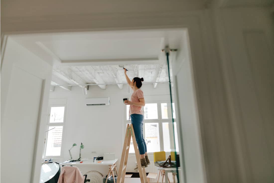 lady on top of a ladder painting the ceiling white. Should You Paint New Textured Ceilings