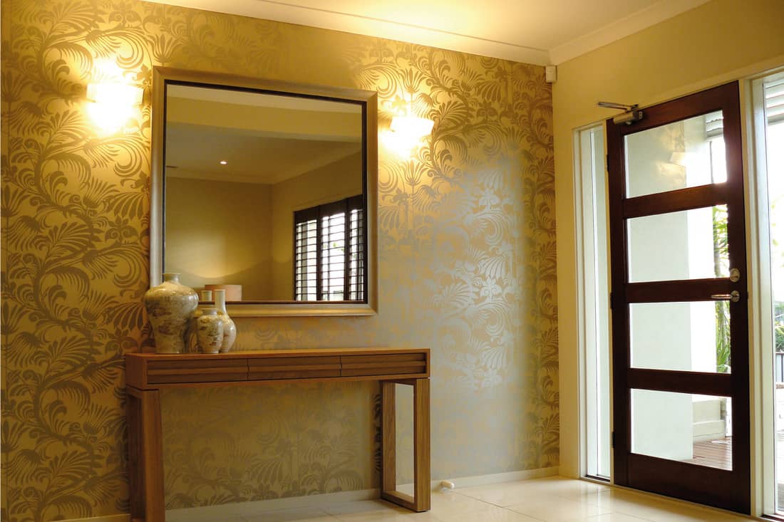 Modern foyer front entrance with gold mirror against gold damask wallpaper