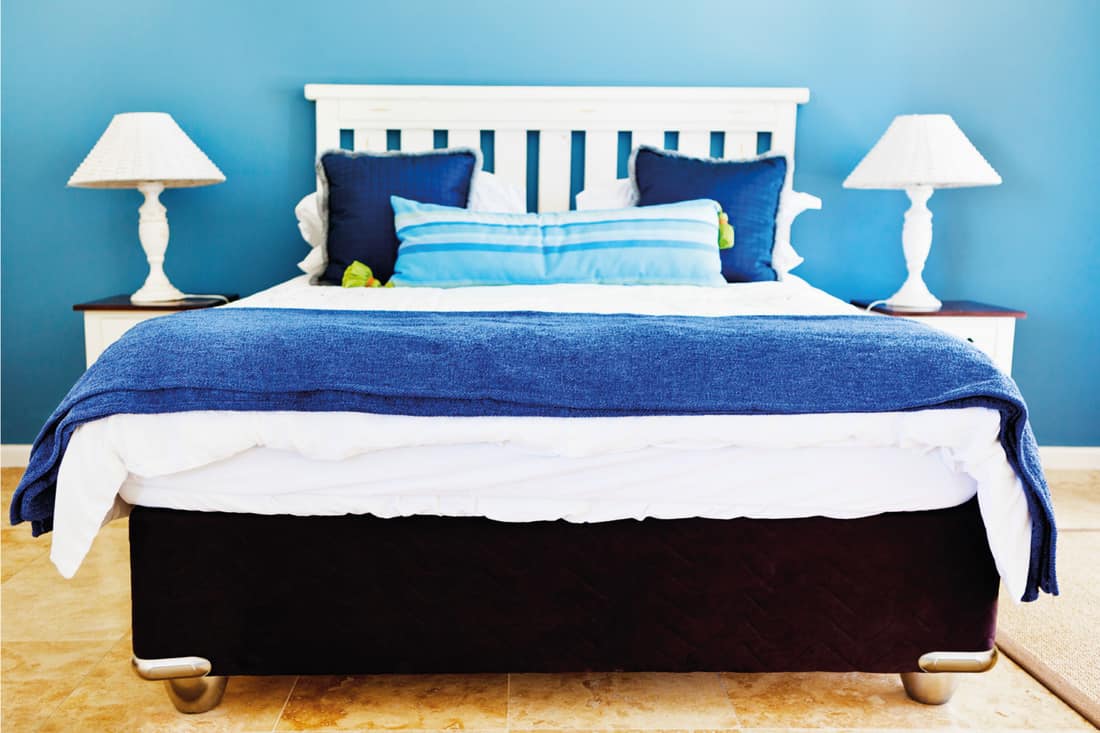 Simple, neat, double bedroom with wooden headboard, bedside tables and lamps, all in shades of blue and white