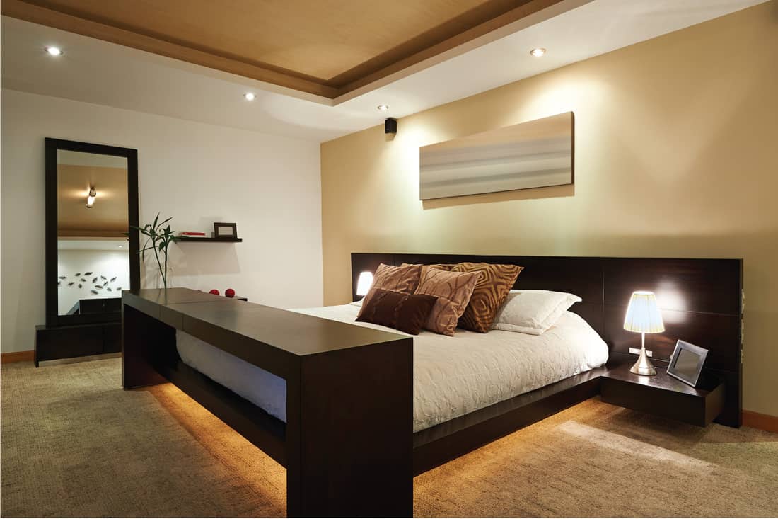 tan bedroom that uses ebony wood finishes and under the bed lighting