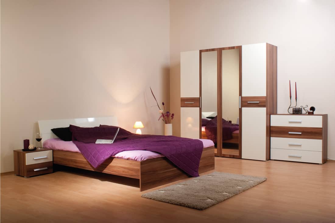 White bed frame in a beige bedroom with purple bedding and wooden accents