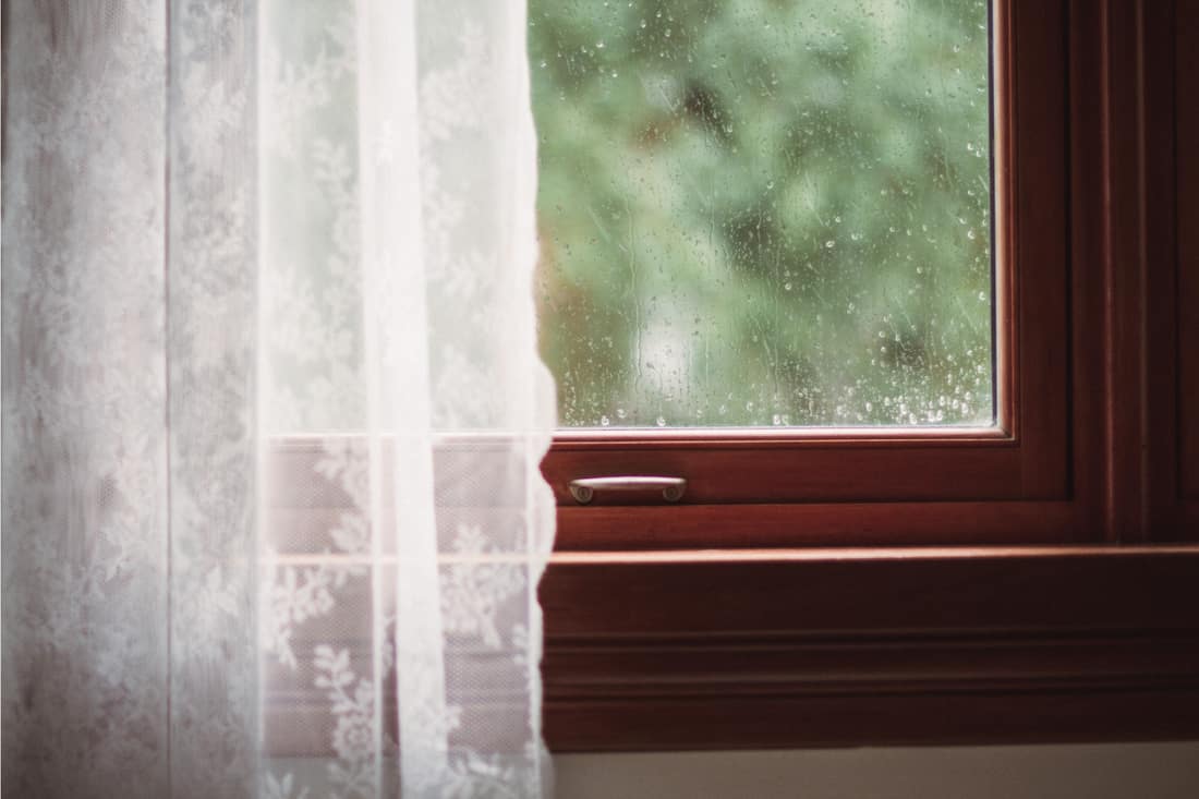 Rideau de dentelle blanche sur une fenêtre en verre avec des éclaboussures d'eau