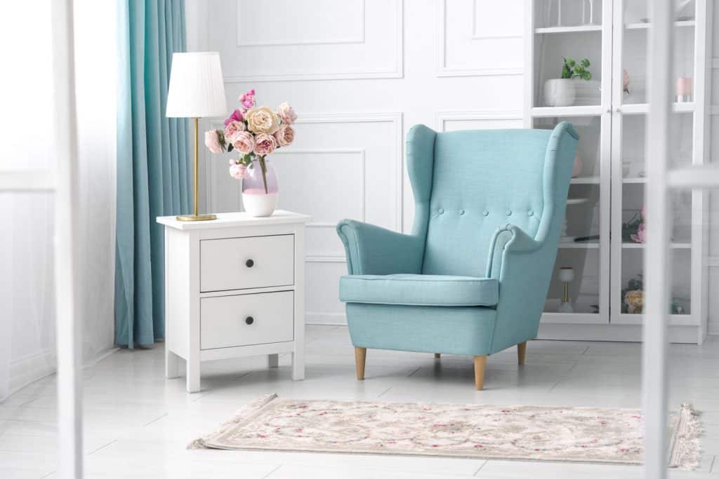 A big light blue colored accent chair with a white end table on the side