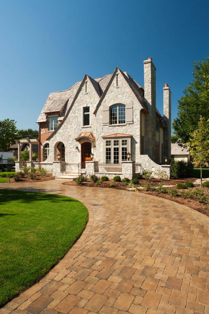 A castle type mansion with brown pavers with bermuda on the driveway