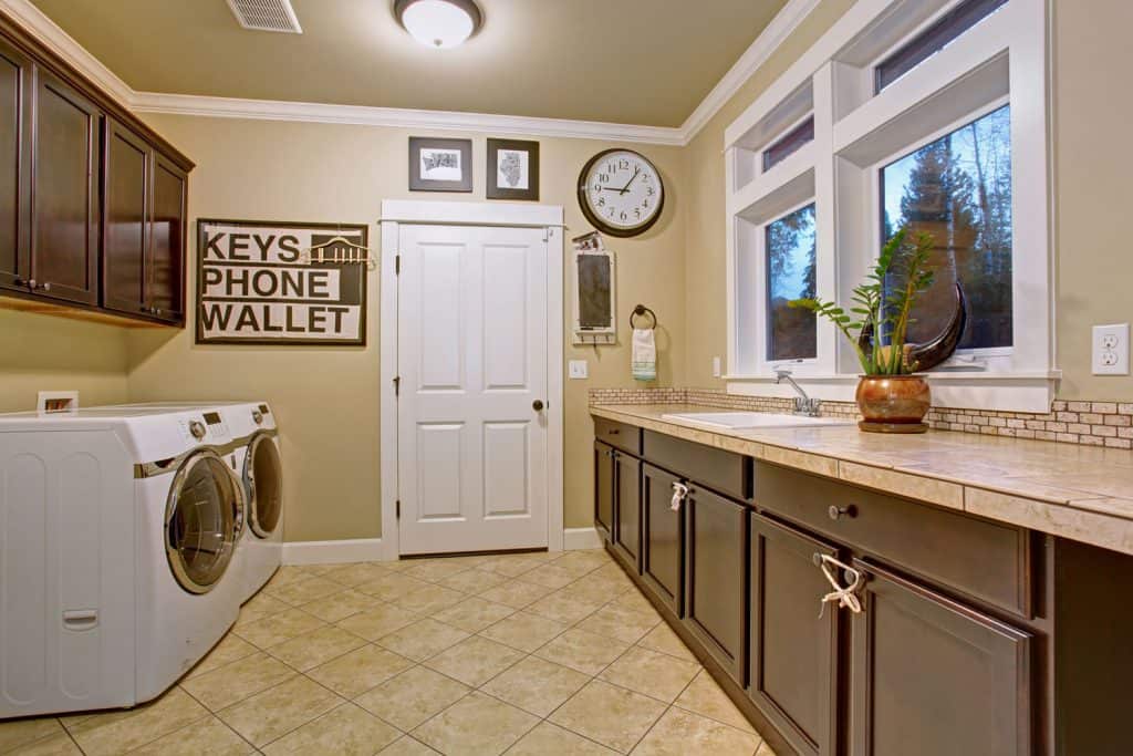 A combined washing area and dining room with cream colored walls and brown painted kitchen cabinets
