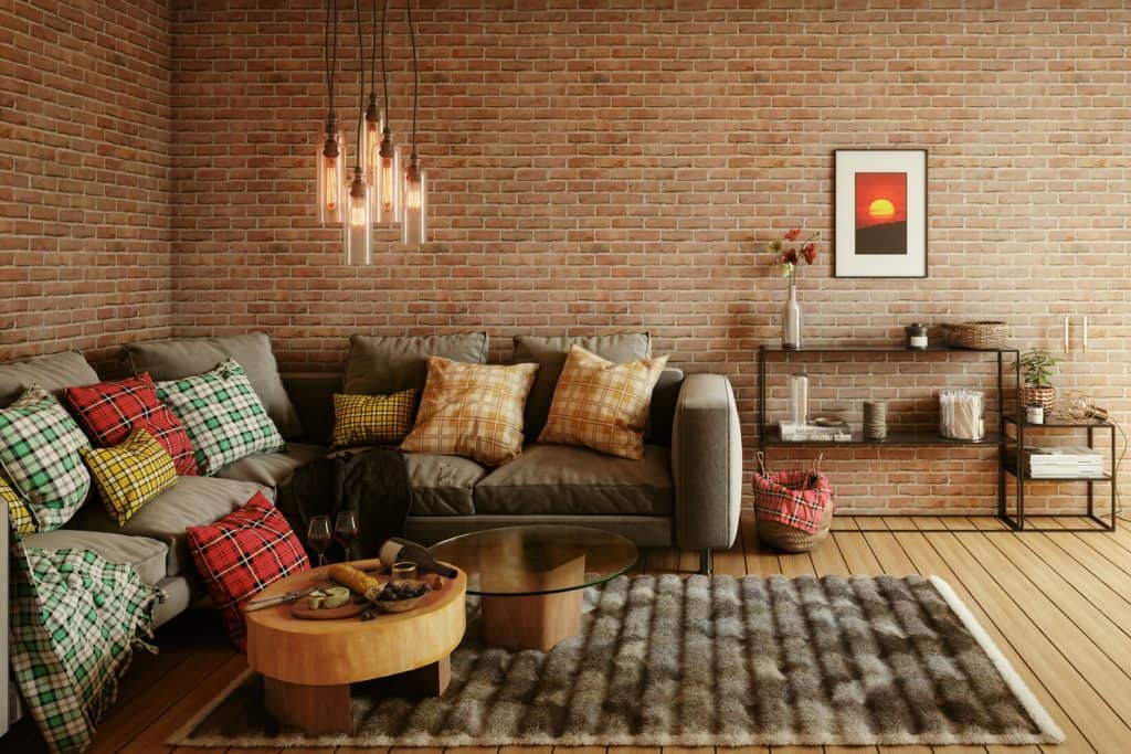 A corner sectional sofa with throw pillows, dangling lamps on top of the round table, and walls made with bricks