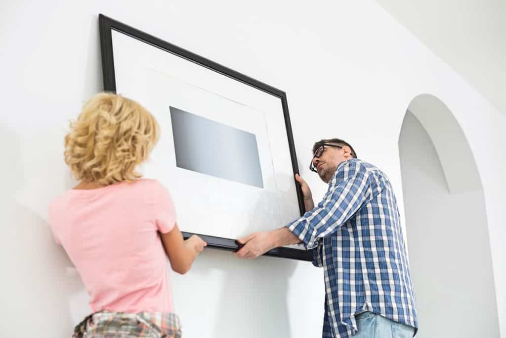 A couple hanging a brand new picture frame on the living room wall
