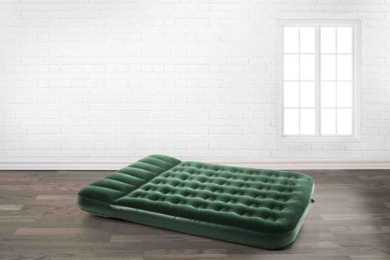 A green air mattress inside a white and empty living room, How To Fix A Hole In An Air Mattress [4 Steps To Follow]