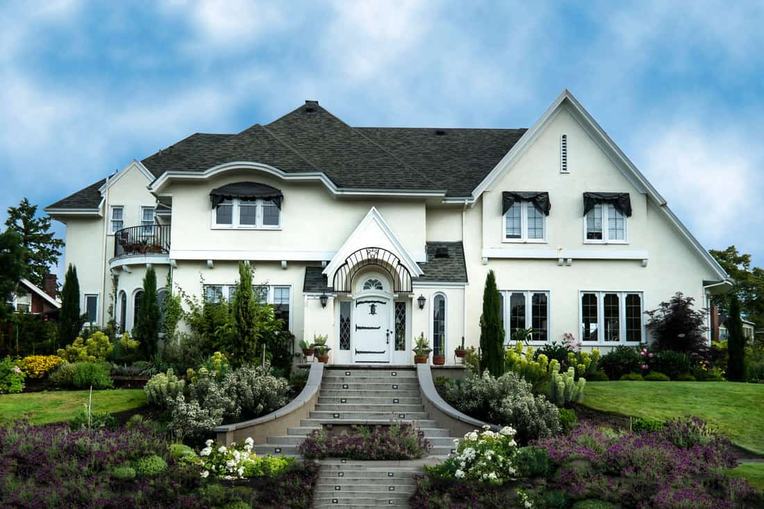 A huge two storey house with white painted exterior wall, black asphalt shingle roofing, and a gorgeous outdoor landscaping, What Color Stucco Goes With Black Roof? [5 Excellent Options Explored!]