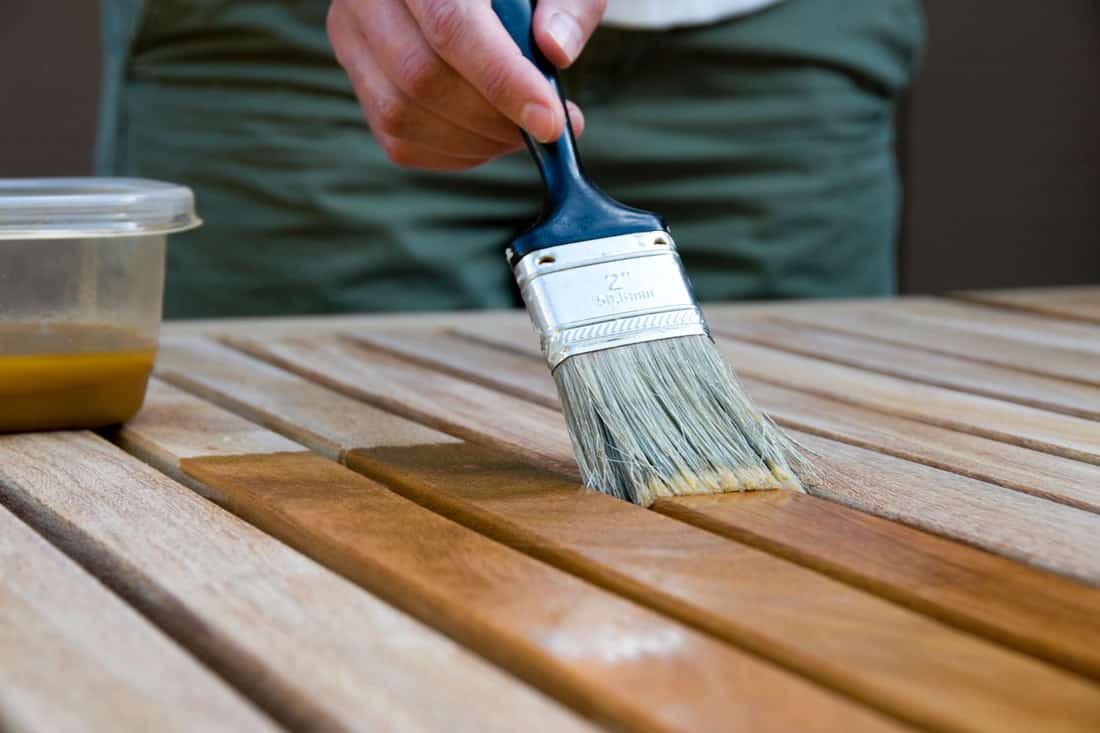 A man brushing the deck with oil to make it look brand new, How To Oil Outdoor Furniture [7 Easy Steps]