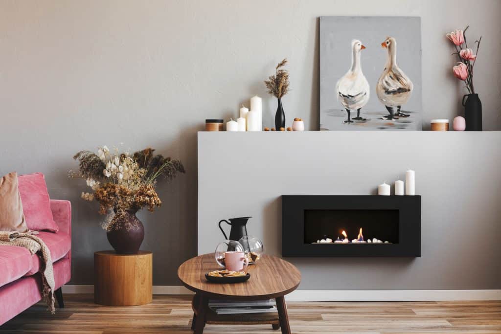 A modern living room with gray painted walls, wooden laminated flooring, a small fireplace with extruded fireplace mantel
