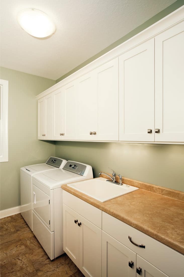 A new house laundry room with white cabinets, tile floor, sink, counter and square door knobs. Opt For Mostly White, But Add A Touch Of Color