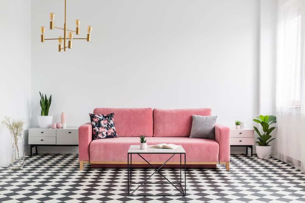 A pink sofa with two throw pillows inside a white walled living room with black and white tiles