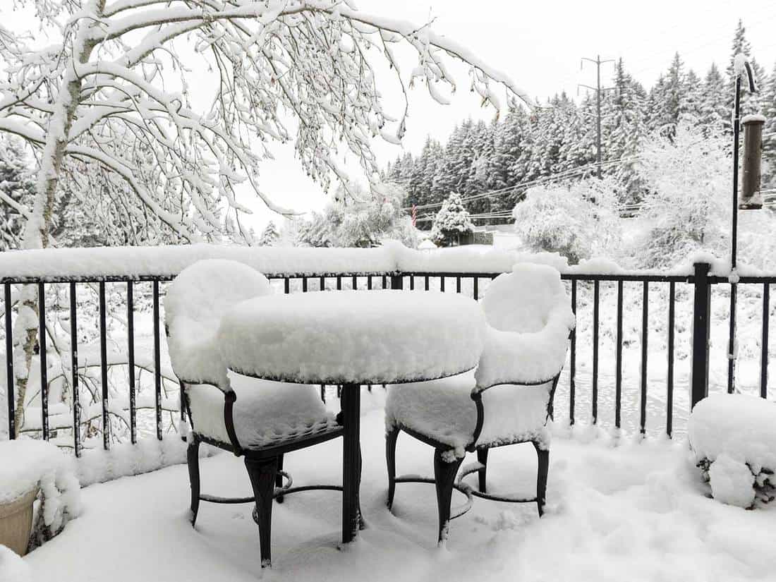 A snow covered deck and furniture