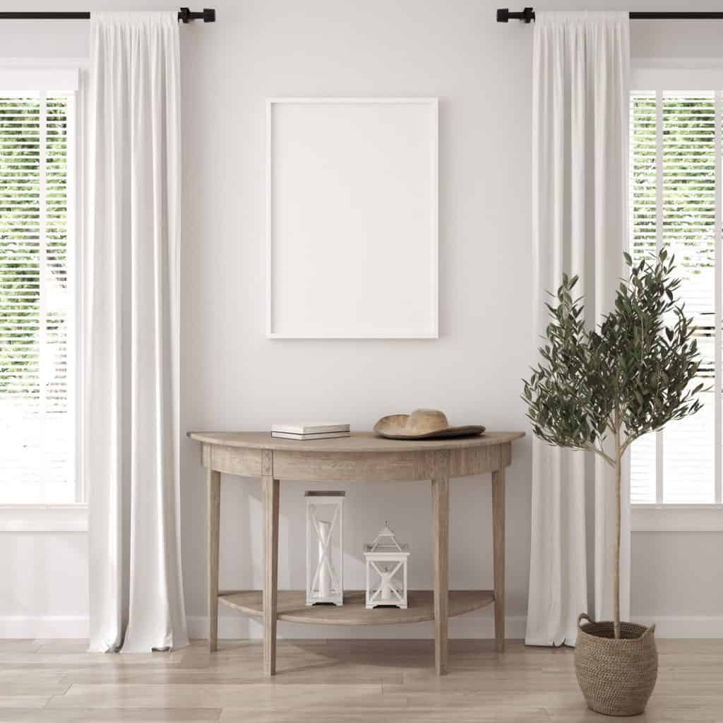 A white walled living room with a white mock up picture frame and a wooden sideboard