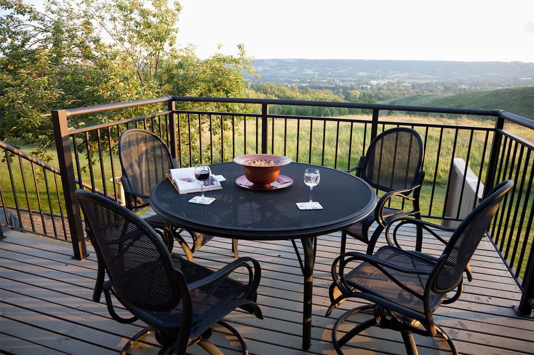 Beautiful sunlight evening. Black Wrought Iron patio furniture. Glass of red and glass of white white on table, What Type Of Outdoor Furniture Lasts Longest?