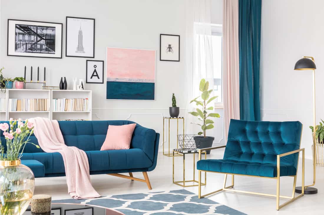 Blue armchair next to settee with pink pillow in sophisticated living room interior with painting