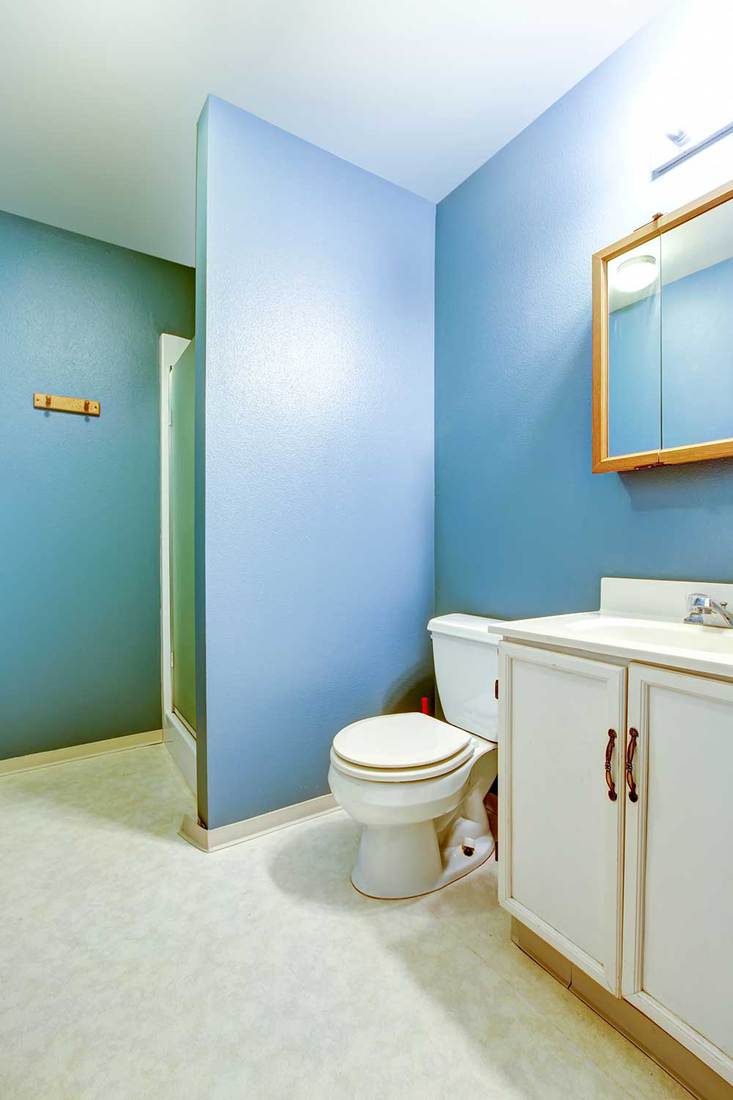 Blue interior of old style bathroom with linoleum flooring, white washbasin cabinet with mirror and toilet