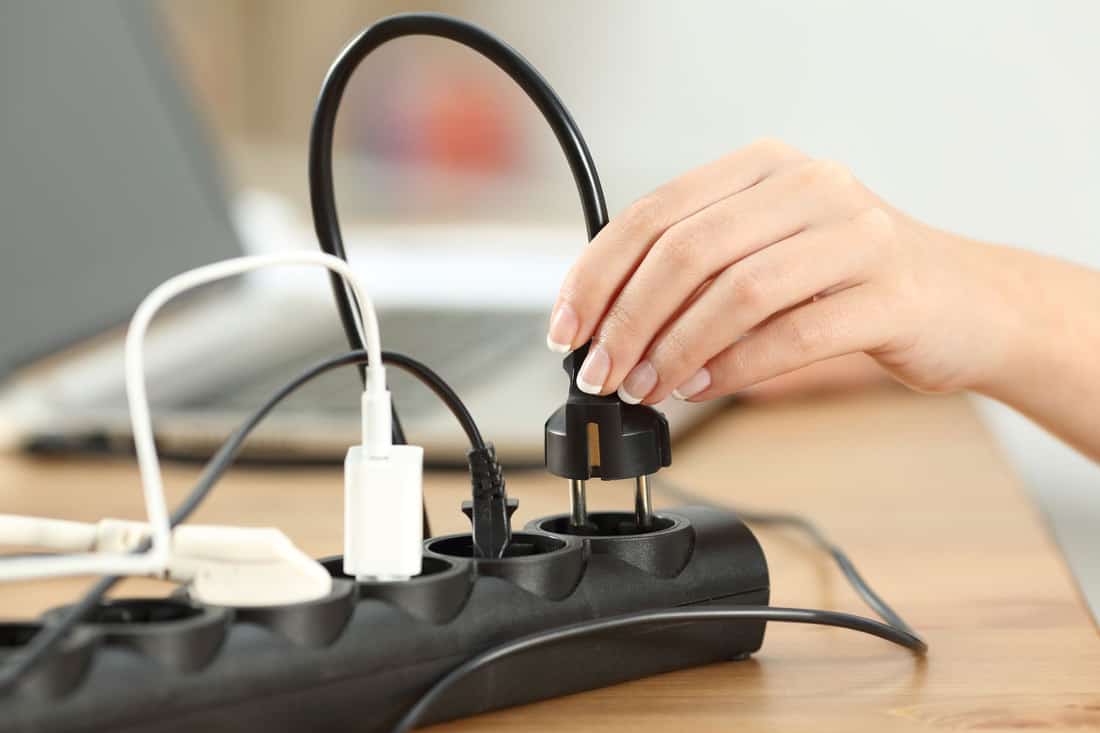Close up of a woman hand plugging a plug in an electrical socket on a table at home
