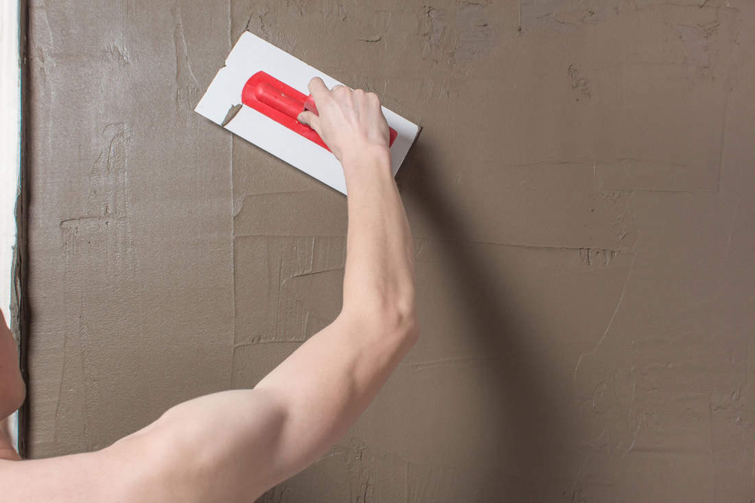 Hand holding a spatula with construction mix.Applying putty or tile glue to the wall, 7 Types Of Stucco Finishes