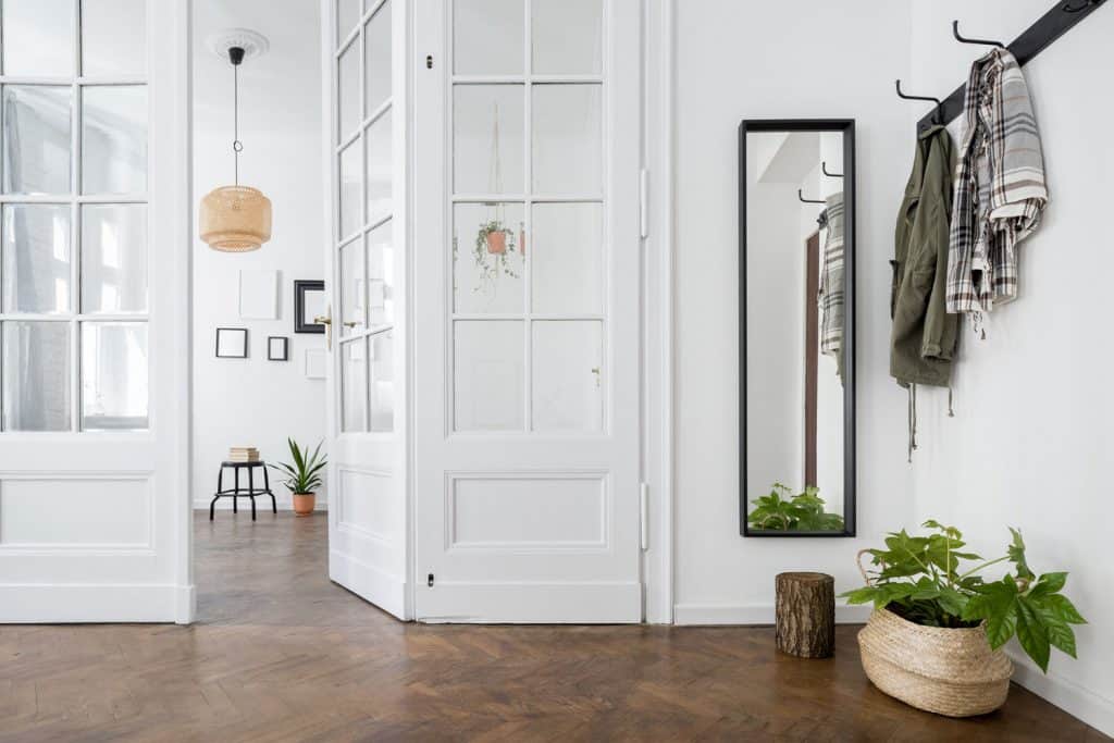 Interior of a Scandinavian themed living room with white painted walls, indoor plants, and a coat rack near the mirror