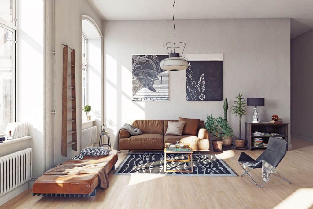 Interior of a Boho-themed living room with picture frames on the wall, brown leather sofa, and a gray patterned carpet on the wooden flooring