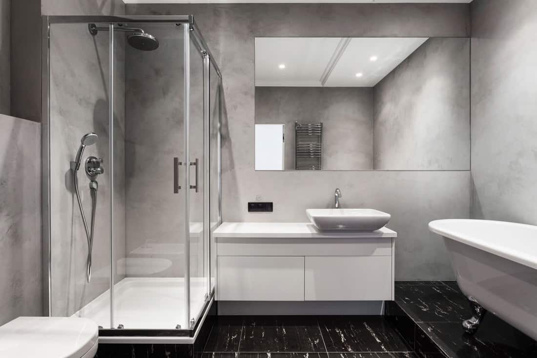 Interior of a modern contemporary living room with gray tiled walls, glass walled shower area with white shower base, and dark patterned tiles, What Are The Standard Sizes For Shower Pans/Bases?
