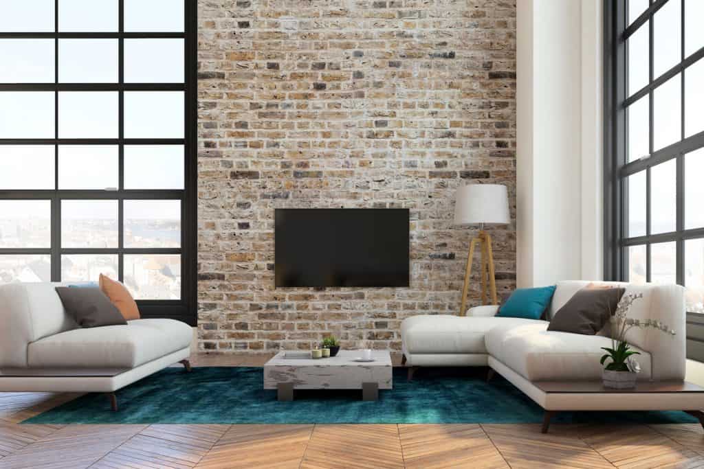 Luxurious modern interior contemporary living room with a decorative brick wall, blue carpet, and white sectional sofas