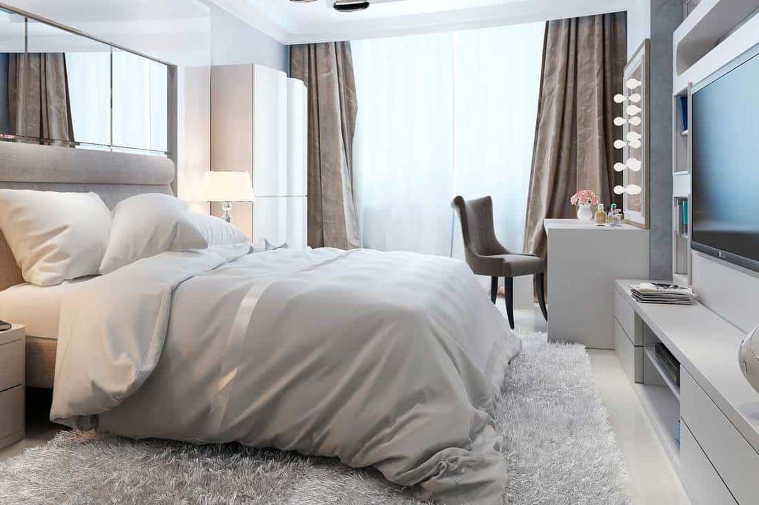 Luxury bedroom interior with cozy bed, vanity, TV and carpet rug on floor, Where To Place A Chair In A Bedroom [6 Amazing Options]