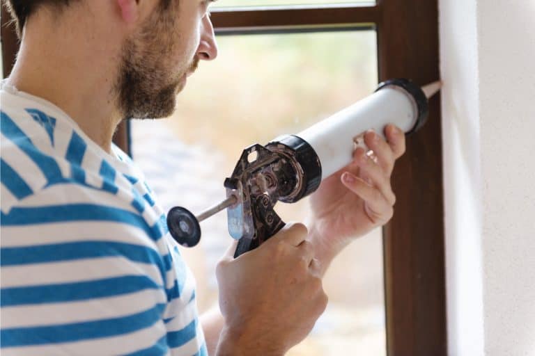Man with caulking gun sealing a window jamb. How Long Does It Take Caulk To Dry Before Painting
