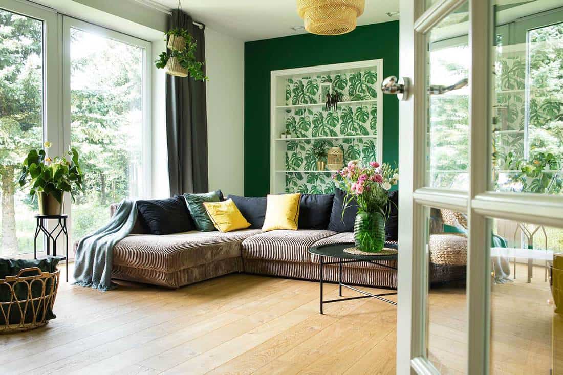 Modern and cozy living room with corduroy sofa, pillows, big window to the garden