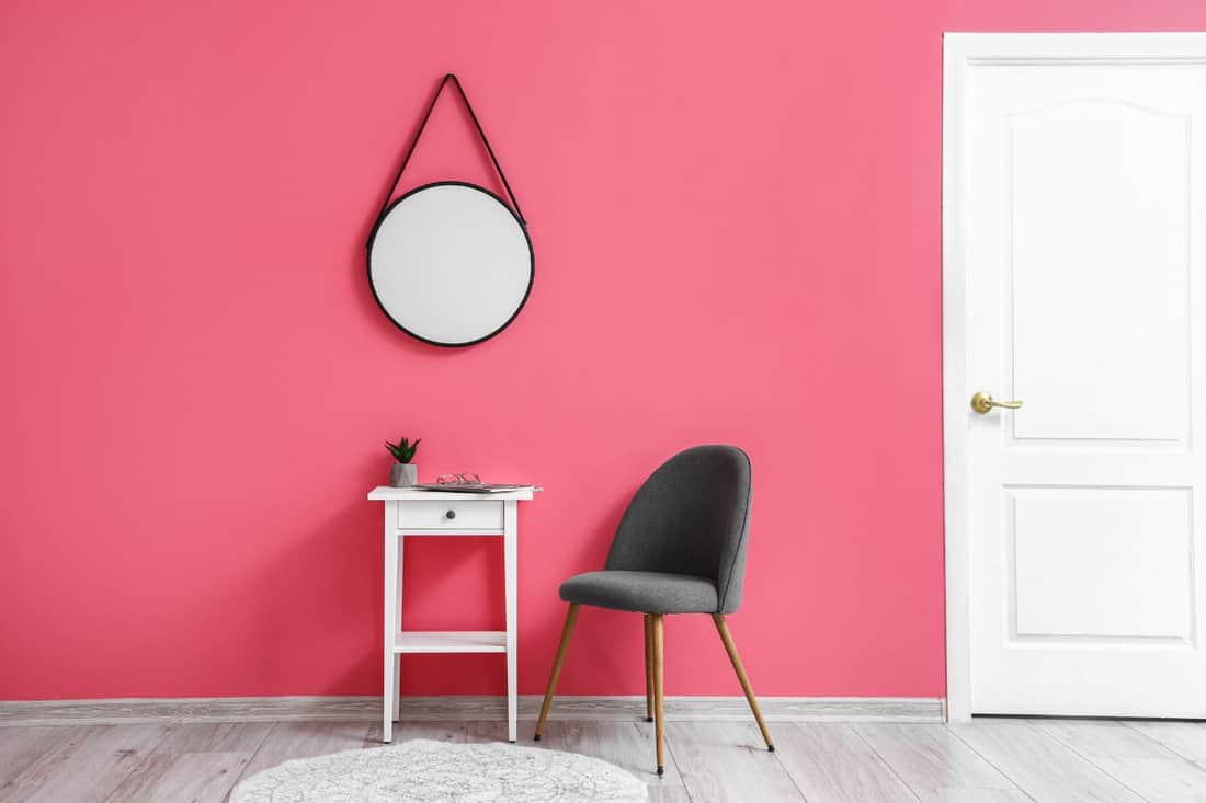 Modern chair with table and mirror near pink wall.