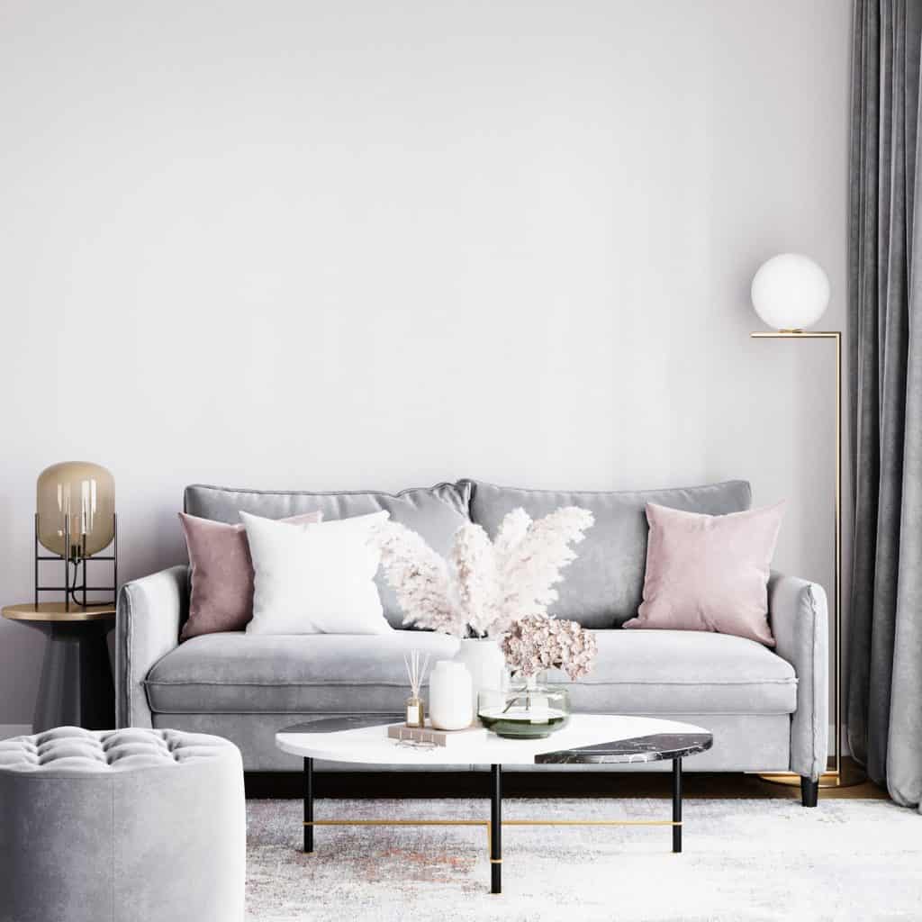 Modern contemporary living room with gray sofa with light pink curtains, gray ottoman, and a round glass coffee table