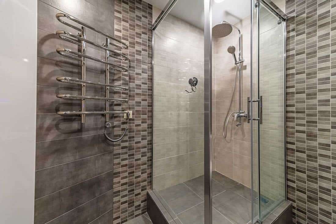 Conception moderne de cabine de douche en verre à l'intérieur de la salle de bains en carreaux marron gris