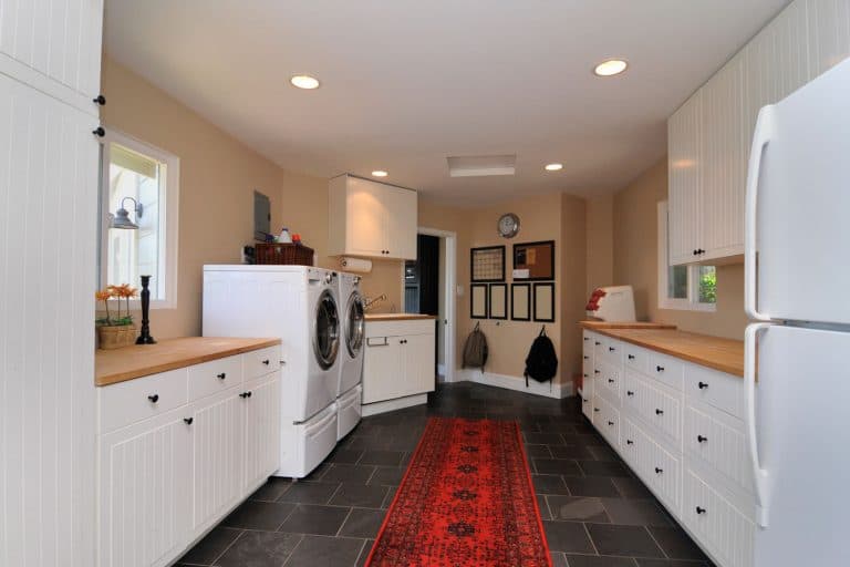 Modern laundry room with white paneled cabinetry, wooden countertop, and two washing machines on the side. 21 Awesome Laundry Room Decor Ideas