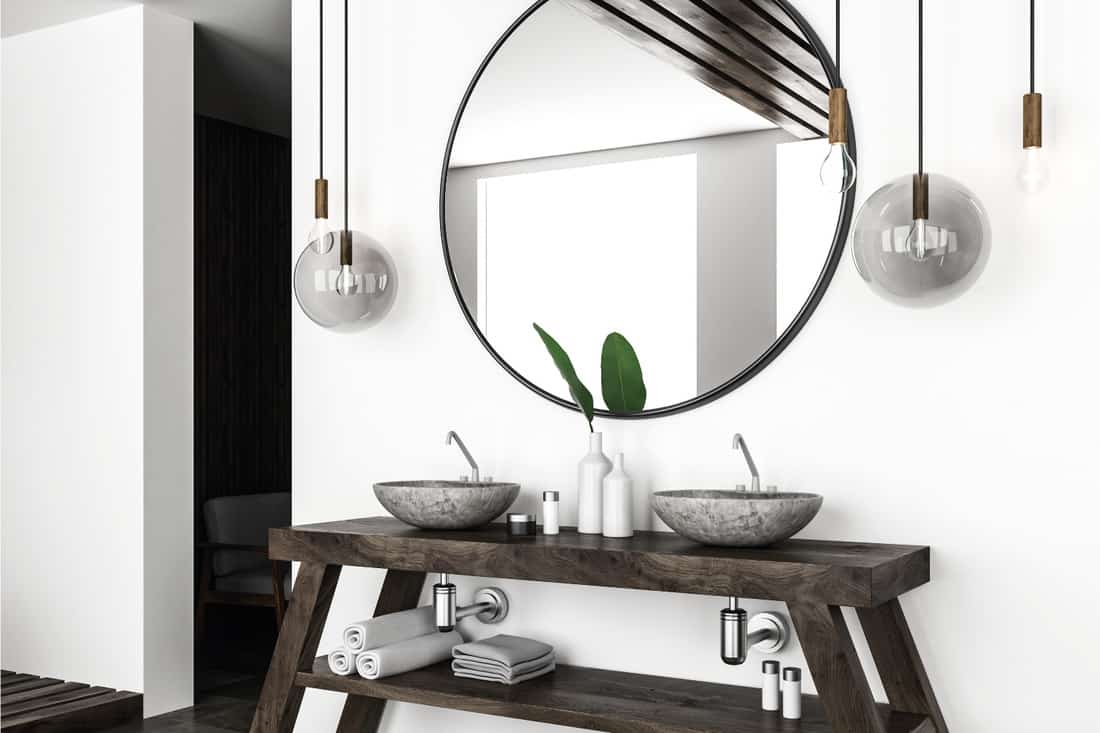 Side view of modern bathroom interior with white walls and stone double sink standing on wooden shelf with big round mirror above it