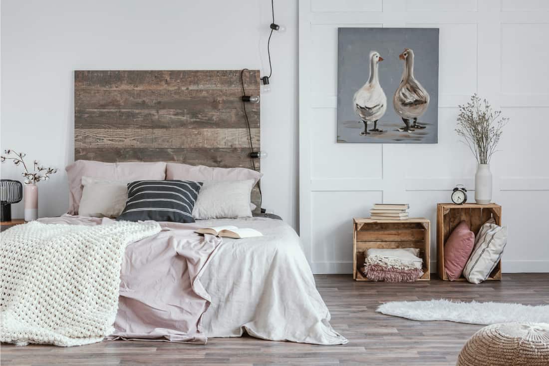 Spacious bedroom interior with rustic furniture, white walls, wooden crates and oil painting of animals.
