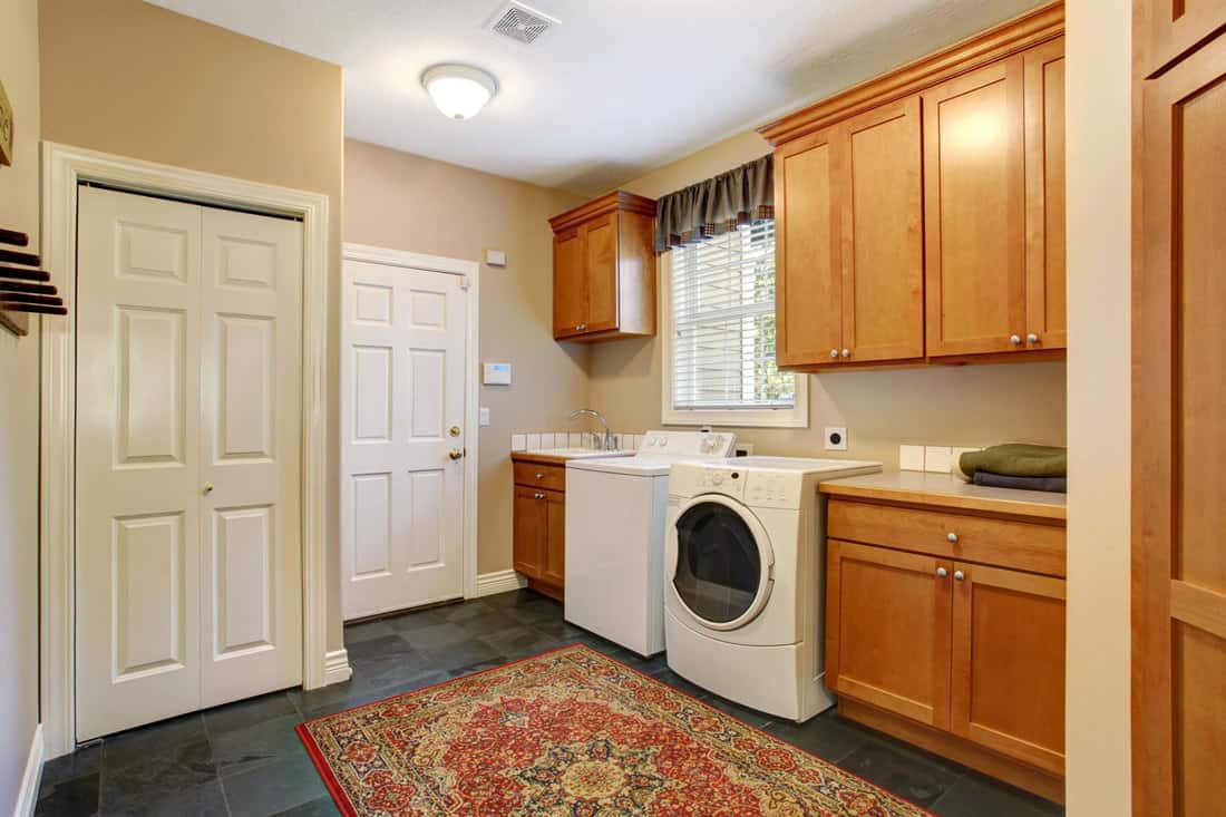 Spacious laundry room with tile floor and rug. Wooden cabinets with white appliannces, Does A Laundry Room Count As Square Footage?