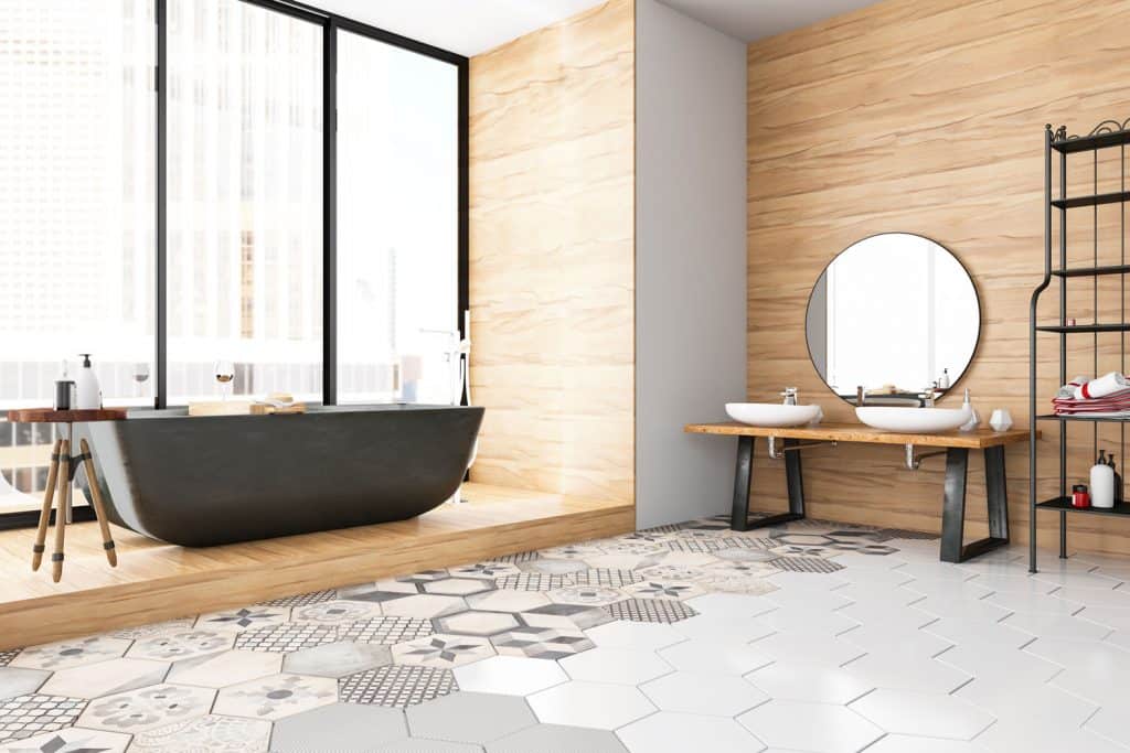Salle de bain spacieuse et moderne avec des murs carrelés en bois, des carreaux à motifs hexagonaux et une immense baignoire noire près de la fenêtre
