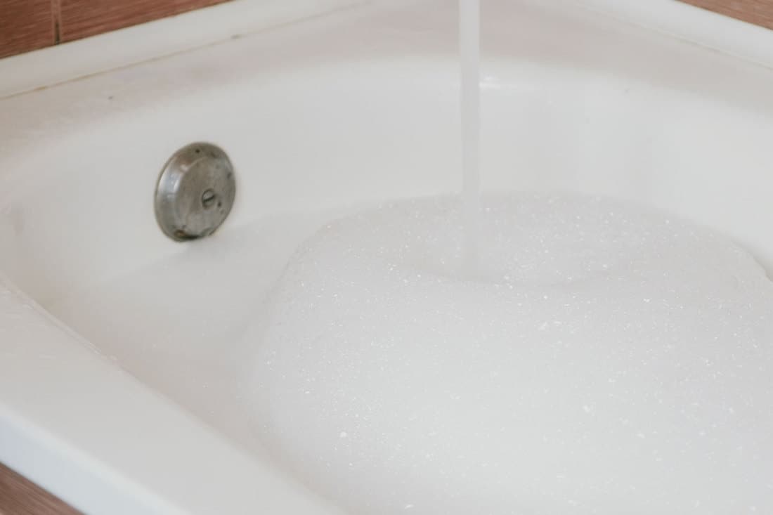 Stream of water pouring into the bath with foam