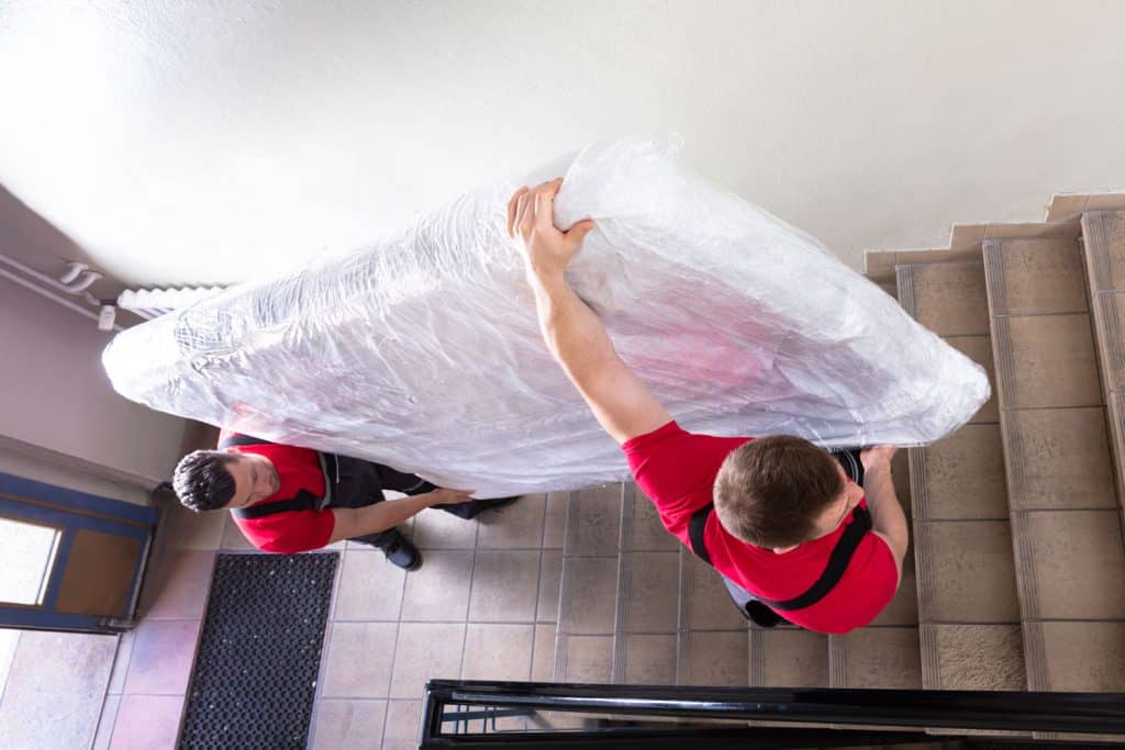 Two movers carrying a huge mattress up the stairs