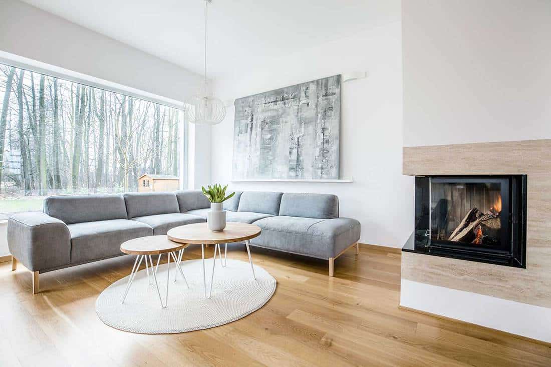 Wooden table on round rug near sofa in spacious living room interior with fireplace and painting