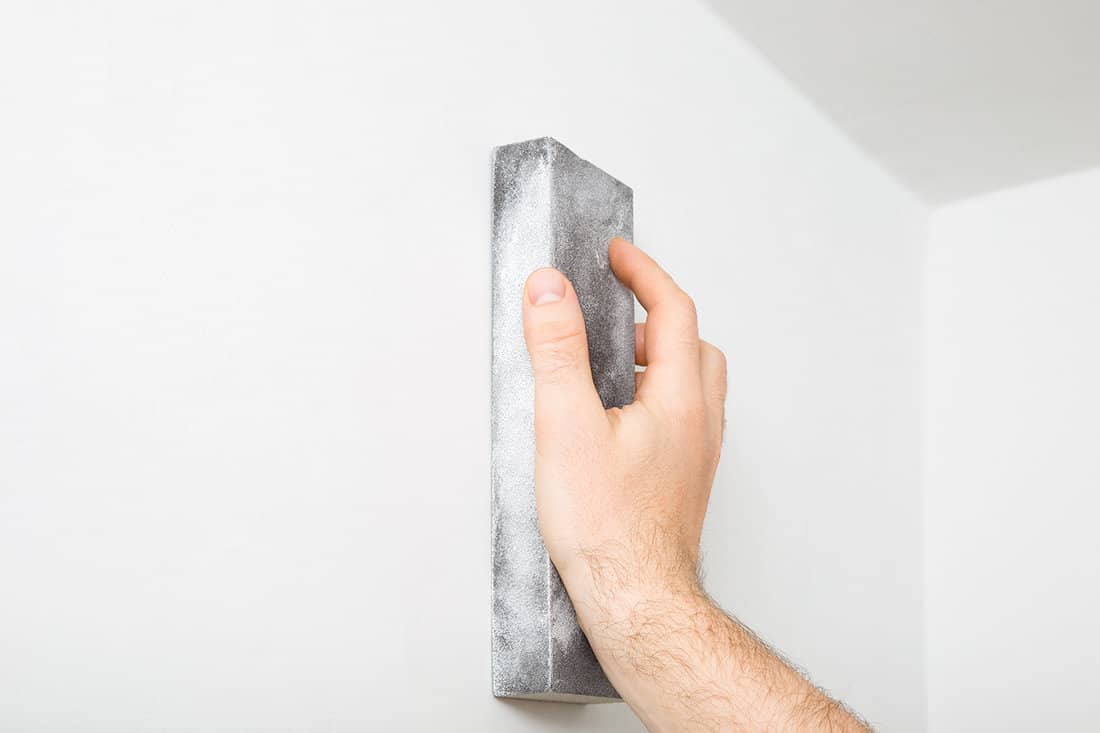 Worker hand polishing white wall with sanding sponge