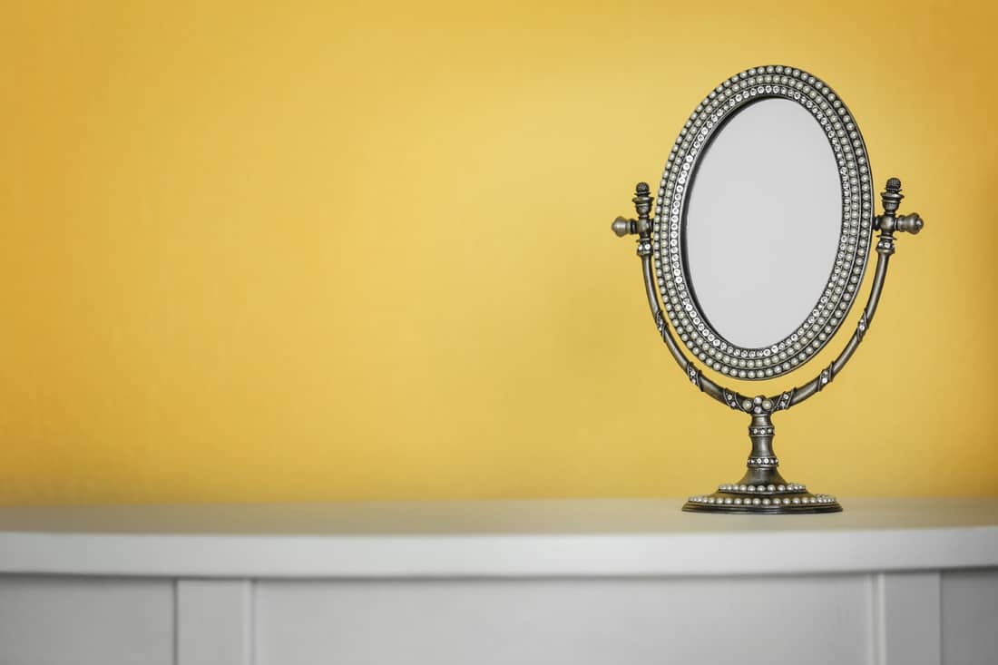 antique mirror on top of a cabinet with a yellow wall background