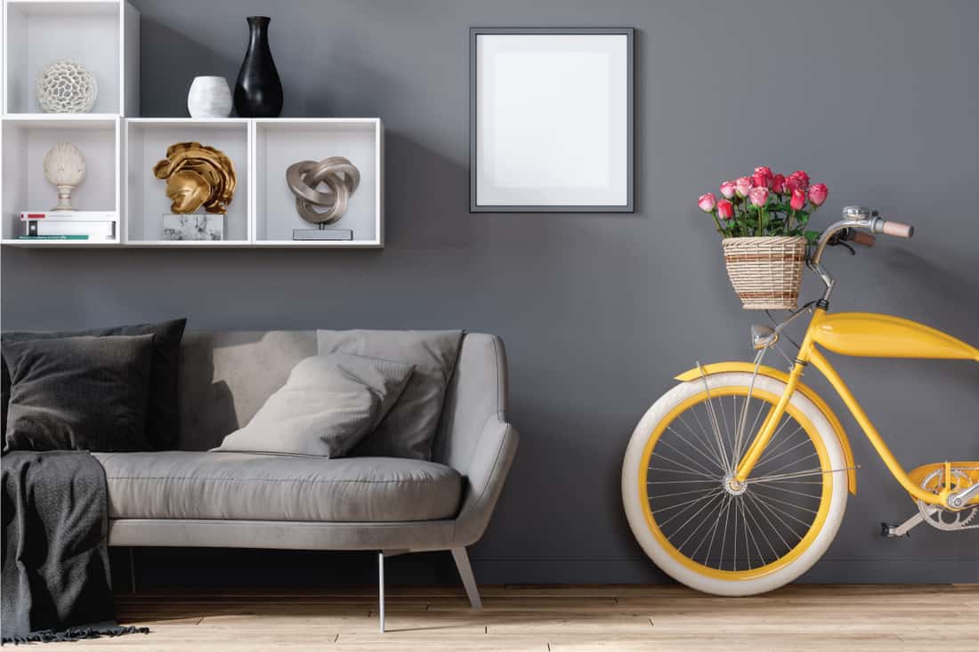 empty gray frame on a gray wall with open bookshelf, gray sofa, yellow bicycle. What Color Picture Frames Go With Grey Walls