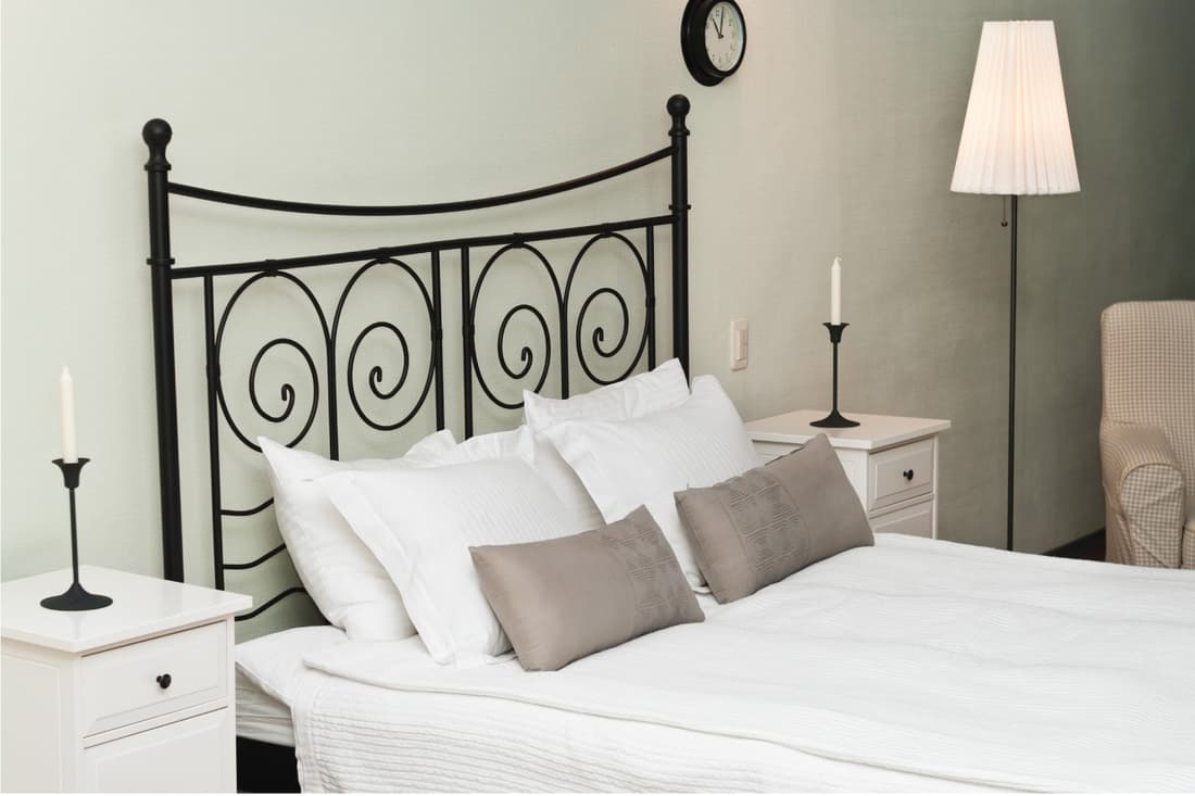 forged metal headboard of bed with pillows. candle stick on nightstand