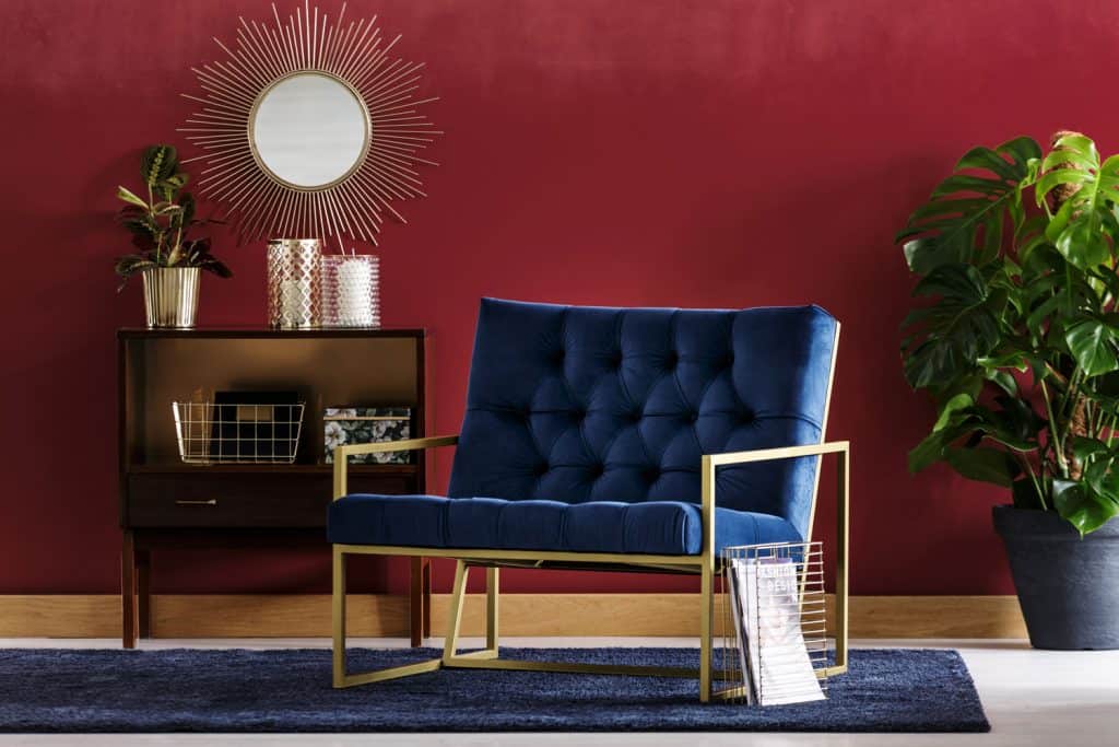 Interior of a modern living room with a red wall, metal framed blue upholstered chair, and a small blue carpet