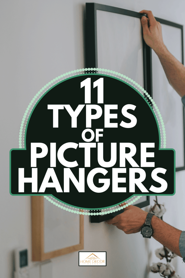 man with beard hanging a painting on the wall at his living room. 11 Types Of Picture Hangers
