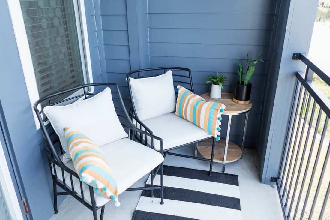 A blue colored porch with metal framed porch chairs with pillows and an end table on the side, 11 Amazing Porch Chair Ideas To Check Out